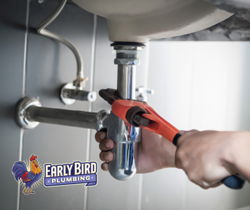 Close-up of a plumber's hands using a pipe wrench to tighten a chrome drain pipe under a sink